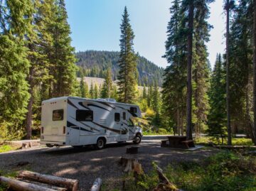 Beautiful campsite in the mountains with an RV and wooden bench.
